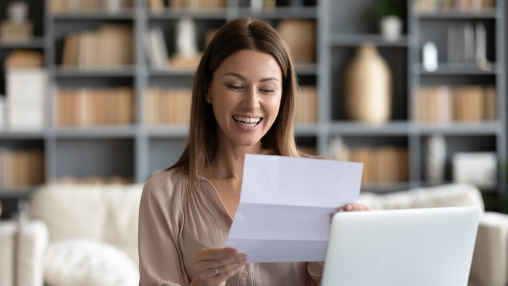 A woman smiling as she reads a letter.