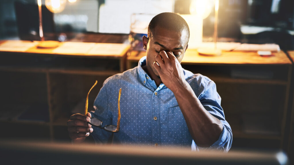 A man pinching the bridge of his nose at work.