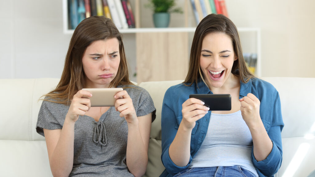 one girl looking envious at the delighted girl next to her on the sofa