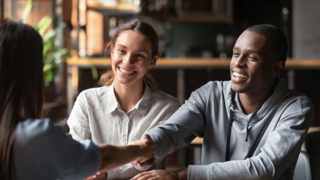 An estate agent shaking hands with a young couple.