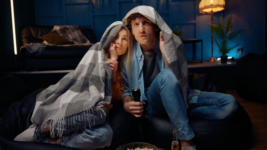 Two people watching a scary movie while hiding under a blanket.