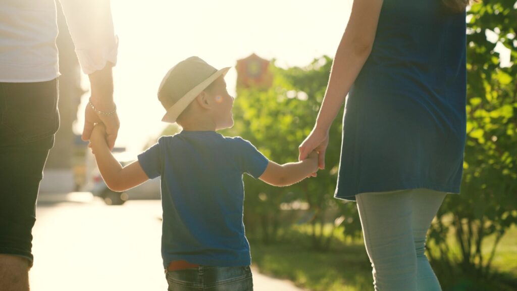 A family with a young child holding hands outdoors.