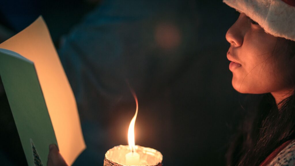 A child singing a Christmas carol by candlelight.