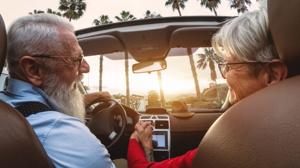 A happy older couple driving in a convertible car.