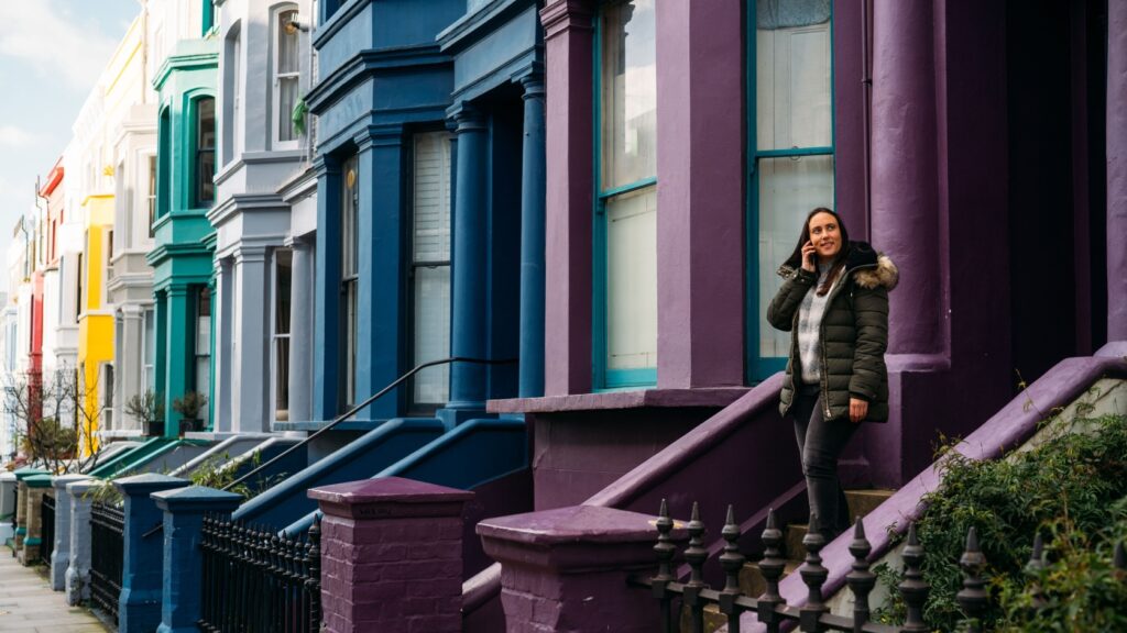 A woman walking out of a front door of a colourful row of terraced housing.