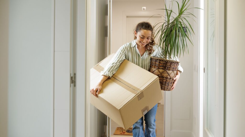 A woman carrying a box and a plant into her new home.