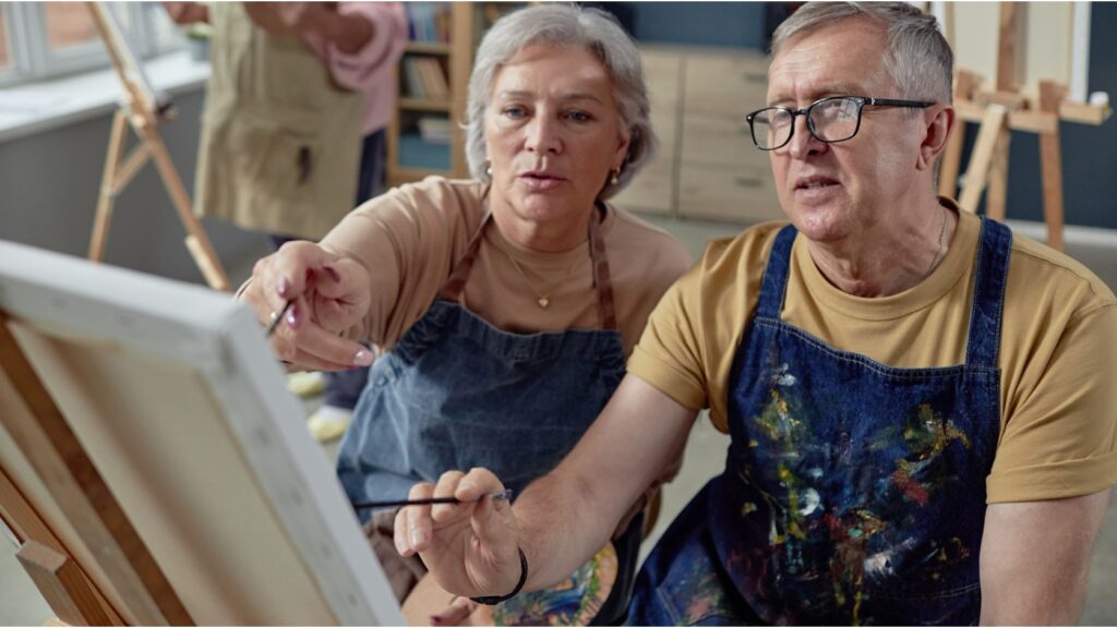 An older couple painting at an easel together.