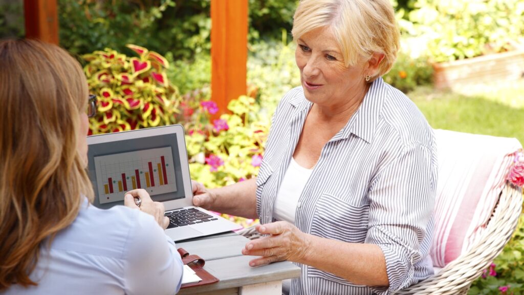 Female financial planner showing a senior woman charts on a laptop